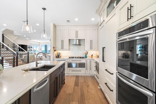 kitchen with hardwood / wood-style floors, appliances with stainless steel finishes, white cabinetry, sink, and wall chimney exhaust hood