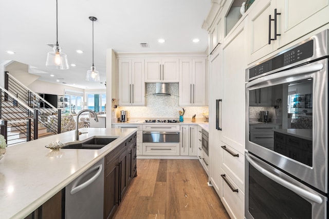 kitchen with visible vents, wall chimney exhaust hood, stainless steel appliances, a warming drawer, and a sink