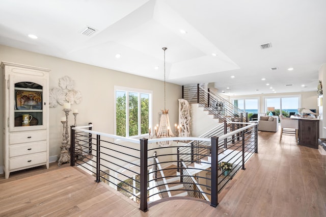 staircase with visible vents, a healthy amount of sunlight, an inviting chandelier, and wood finished floors