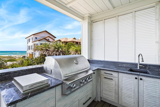 view of patio with an outdoor kitchen, area for grilling, a sink, a water view, and a beach view