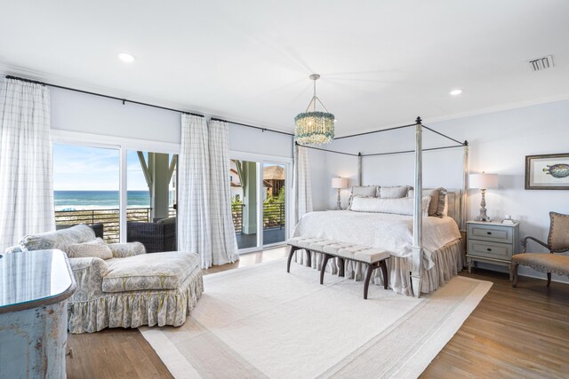 bedroom featuring hardwood / wood-style flooring, a chandelier, a water view, and access to exterior