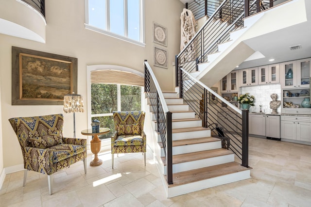 stairs featuring visible vents, baseboards, a high ceiling, and stone finish flooring