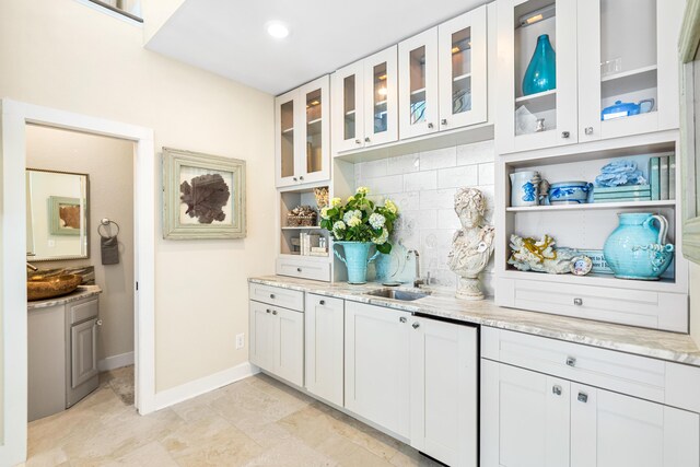 kitchen featuring glass insert cabinets, baseboards, light stone counters, decorative backsplash, and a sink