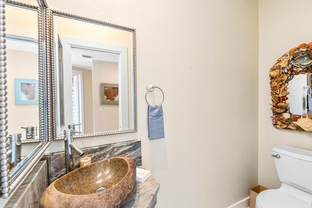 half bathroom with toilet, baseboards, visible vents, and a sink
