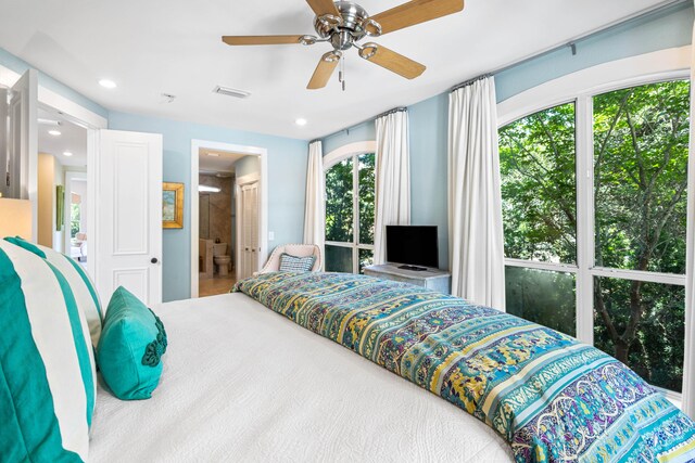 bedroom featuring ceiling fan, ensuite bathroom, and multiple windows