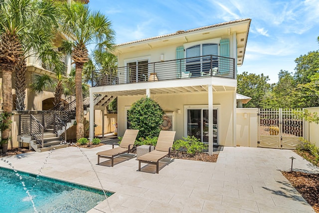 rear view of house featuring stucco siding, a gate, a patio, fence, and a balcony