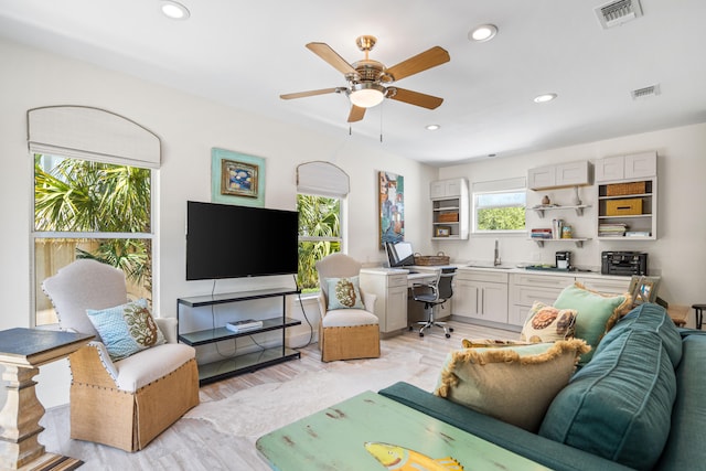 living room featuring light wood-type flooring, built in desk, sink, and ceiling fan