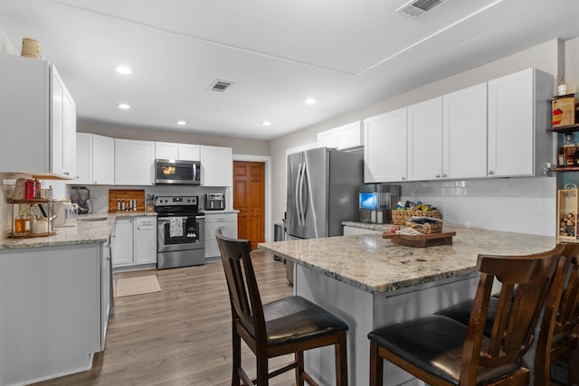 kitchen with light wood-type flooring, light stone counters, stainless steel appliances, white cabinetry, and a breakfast bar