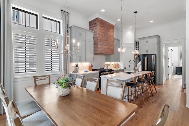 dining area with crown molding, sink, light wood-type flooring, and an inviting chandelier