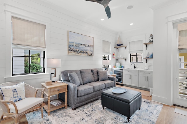 living room with wine cooler, light hardwood / wood-style floors, indoor wet bar, ceiling fan, and wooden walls