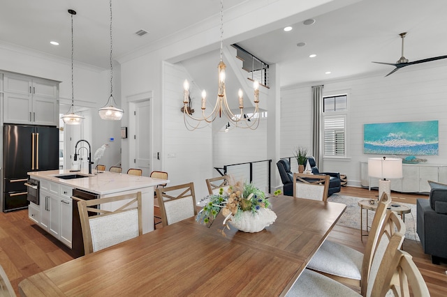 dining area with crown molding, sink, ceiling fan with notable chandelier, and light wood-type flooring