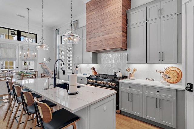 kitchen with stainless steel range, decorative light fixtures, an island with sink, light stone countertops, and a breakfast bar