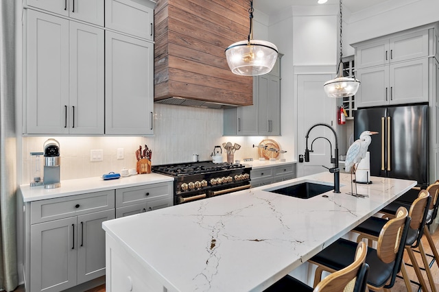 kitchen featuring high end appliances, decorative light fixtures, a kitchen island with sink, ornamental molding, and sink