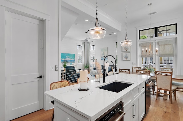 kitchen with decorative light fixtures, light hardwood / wood-style flooring, a kitchen island with sink, sink, and white cabinetry