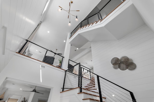 staircase featuring ceiling fan with notable chandelier and high vaulted ceiling