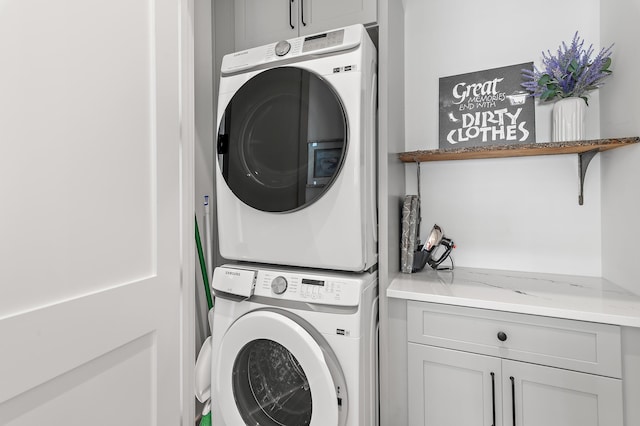 clothes washing area with stacked washer and clothes dryer and cabinets