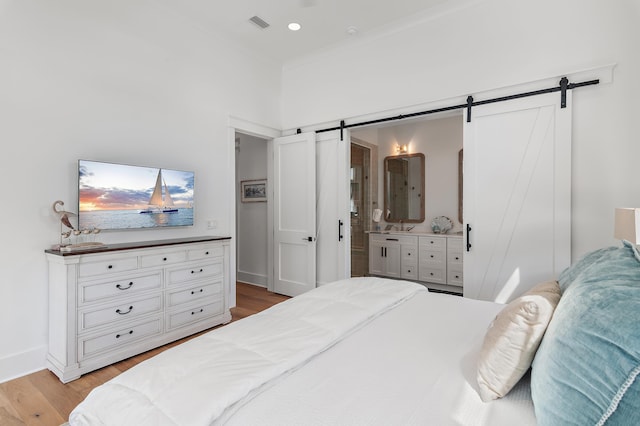 bedroom with a barn door, light wood-type flooring, connected bathroom, and crown molding