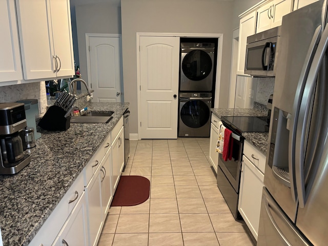 kitchen with white cabinets, sink, appliances with stainless steel finishes, stacked washer / drying machine, and decorative backsplash