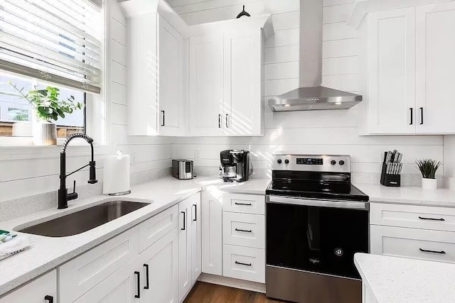 kitchen with stainless steel electric stove, light stone countertops, sink, wall chimney range hood, and white cabinets