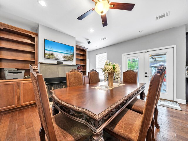 dining area featuring dark wood-type flooring, ceiling fan, a fireplace, and french doors