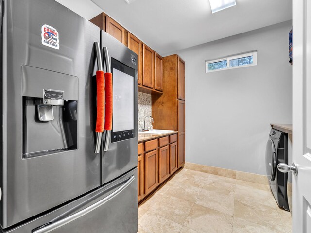 kitchen with stainless steel refrigerator with ice dispenser, washer / dryer, tasteful backsplash, and sink