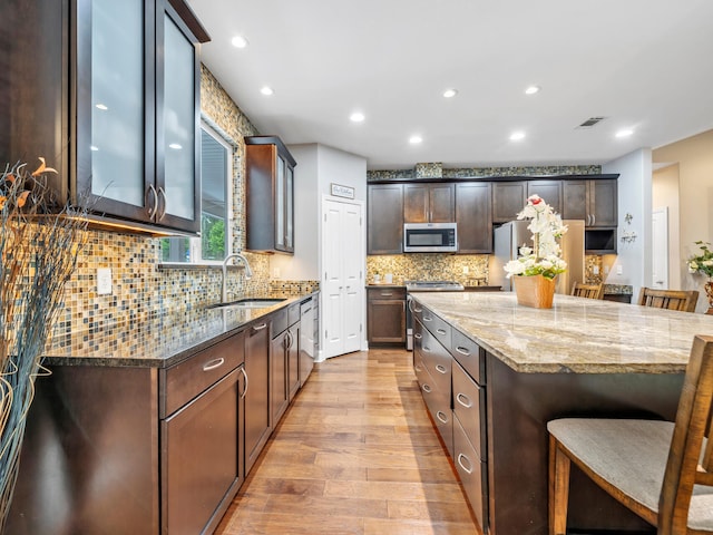 kitchen with backsplash, stone counters, stainless steel appliances, light hardwood / wood-style floors, and sink