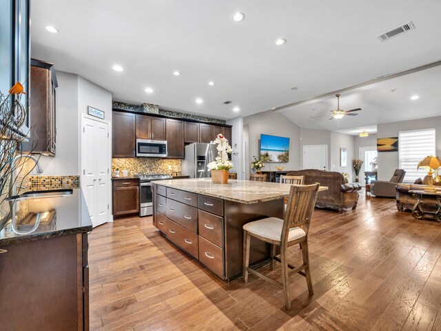 kitchen with appliances with stainless steel finishes, light stone countertops, light hardwood / wood-style floors, ceiling fan, and a kitchen island