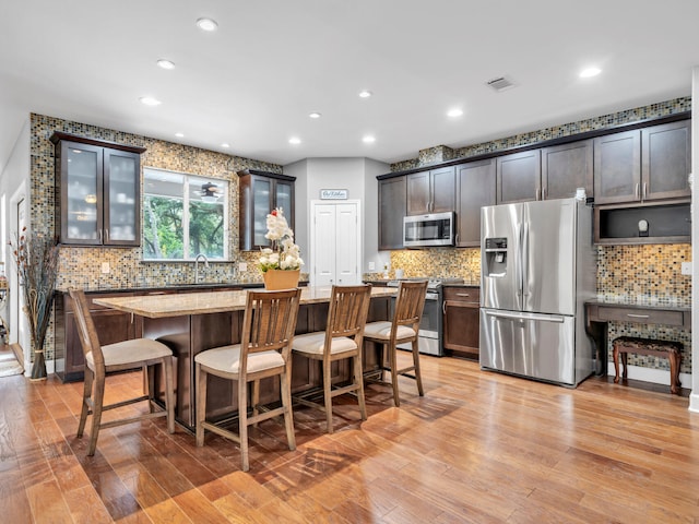 kitchen with light hardwood / wood-style flooring, backsplash, light stone countertops, appliances with stainless steel finishes, and dark brown cabinetry