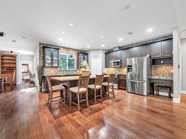 kitchen featuring a kitchen island, stainless steel appliances, wood-type flooring, a kitchen breakfast bar, and backsplash