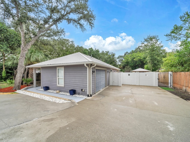 view of side of property featuring a garage, driveway, a gate, fence, and metal roof