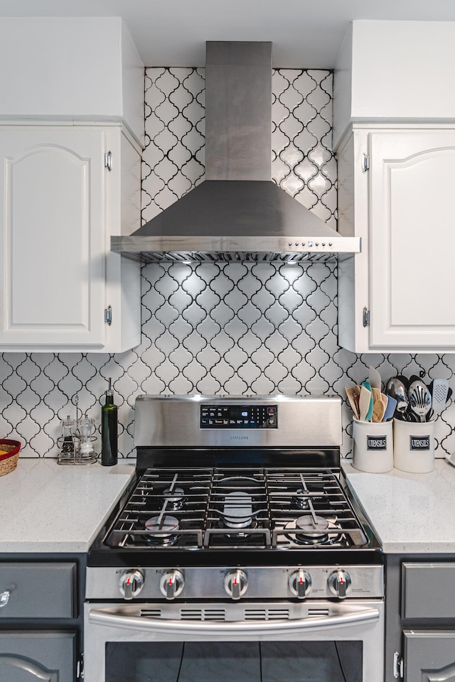 kitchen featuring wall chimney exhaust hood, stainless steel range with gas cooktop, tasteful backsplash, and white cabinetry