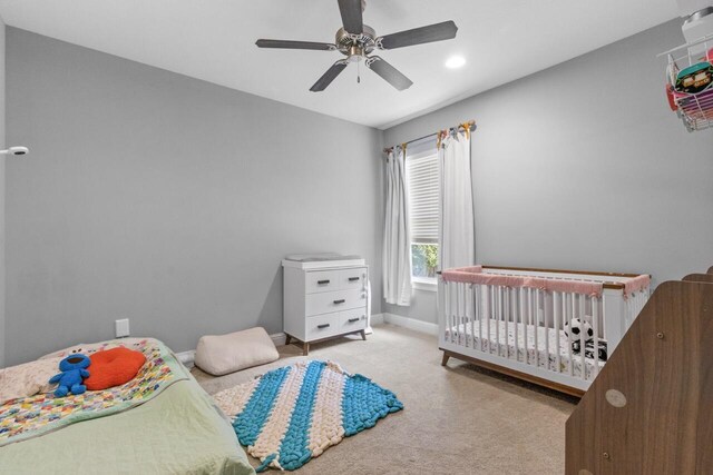 carpeted bedroom with ceiling fan and a nursery area