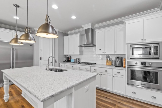 kitchen featuring built in appliances, sink, white cabinets, and wall chimney range hood