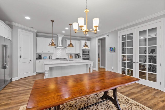 kitchen with a kitchen island with sink, pendant lighting, white cabinetry, appliances with stainless steel finishes, and wall chimney range hood