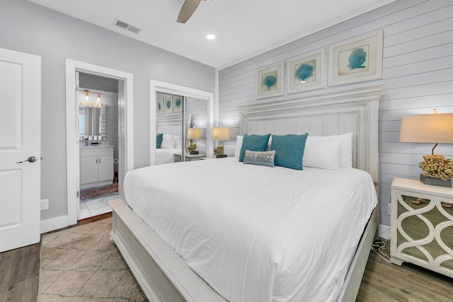 bedroom featuring ceiling fan, wood walls, hardwood / wood-style flooring, a closet, and ensuite bath