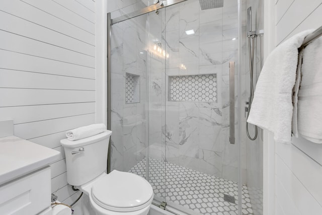 bathroom with vanity, wood walls, a shower with shower door, and toilet