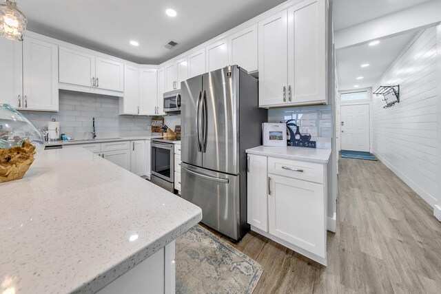 kitchen with appliances with stainless steel finishes, light wood-type flooring, light stone countertops, and white cabinetry