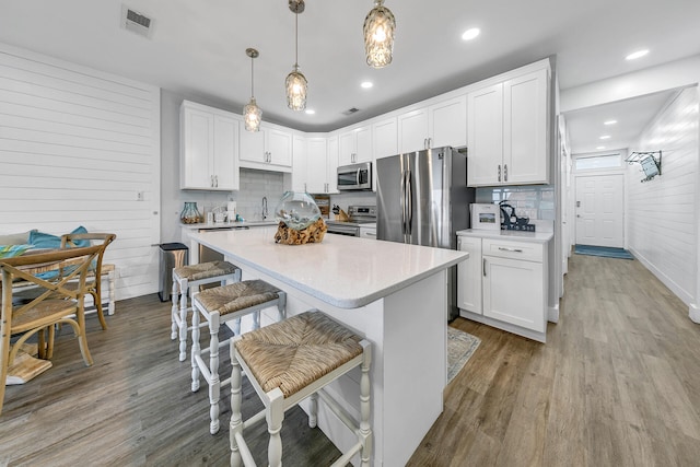 kitchen featuring appliances with stainless steel finishes, tasteful backsplash, white cabinets, pendant lighting, and light hardwood / wood-style flooring