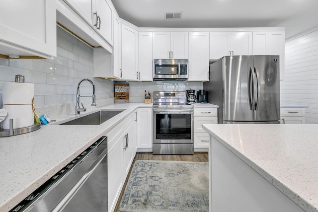 kitchen with stainless steel appliances, light stone counters, white cabinets, and sink