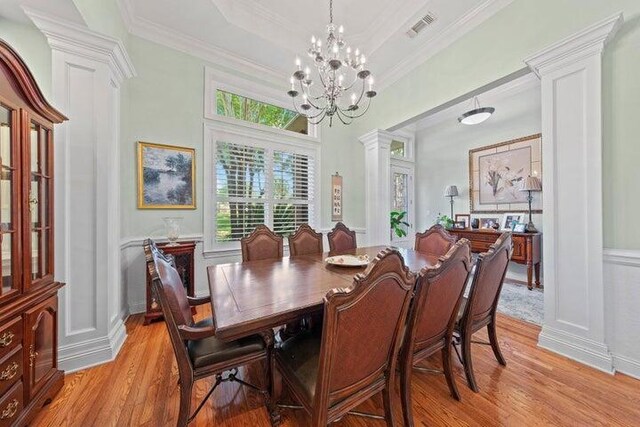 dining area featuring a chandelier, crown molding, decorative columns, and light hardwood / wood-style floors