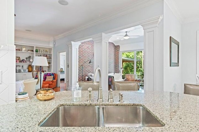 kitchen with light stone countertops, ceiling fan, ornamental molding, and sink