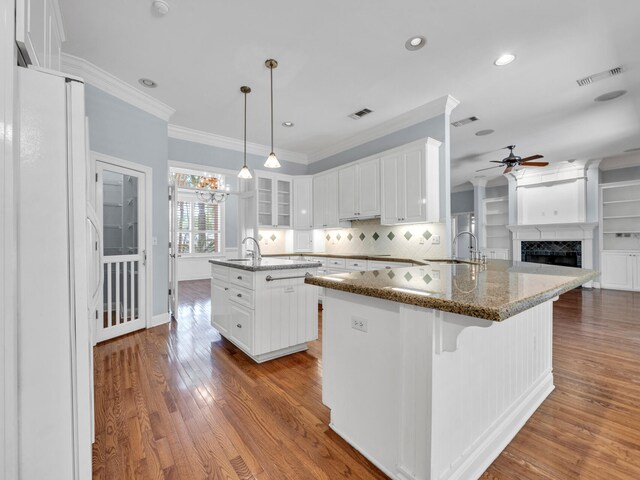 kitchen featuring crown molding, an island with sink, wood-type flooring, decorative light fixtures, and white cabinets