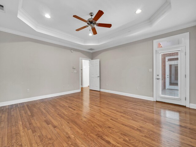 empty room featuring a tray ceiling, crown molding, ceiling fan, and wood-type flooring