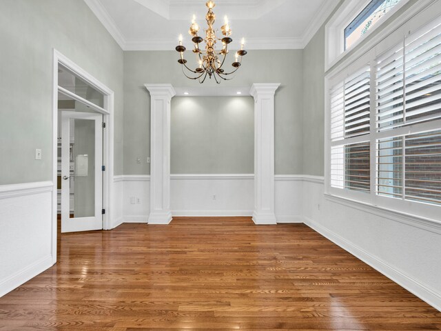 unfurnished dining area featuring hardwood / wood-style floors, a notable chandelier, crown molding, and decorative columns