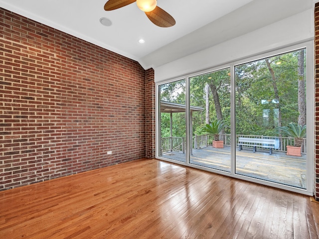 unfurnished room with hardwood / wood-style flooring, ceiling fan, brick wall, and a wealth of natural light