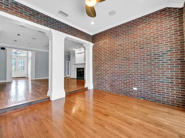 unfurnished living room with ceiling fan, light wood-type flooring, ornamental molding, and brick wall