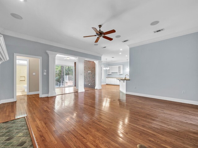 unfurnished living room featuring decorative columns, ceiling fan, ornamental molding, and hardwood / wood-style flooring