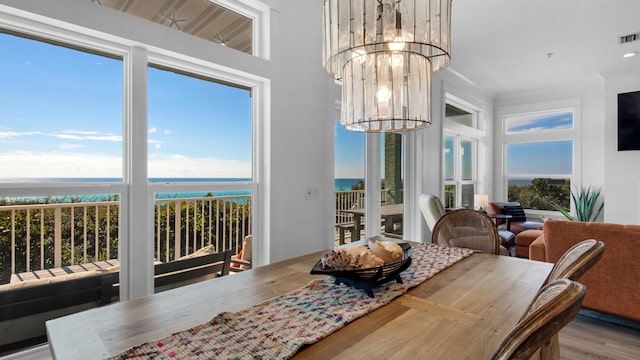 dining room with plenty of natural light, a water view, light hardwood / wood-style flooring, and an inviting chandelier