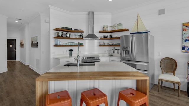 kitchen with dark hardwood / wood-style flooring, wall chimney exhaust hood, a breakfast bar, stainless steel appliances, and crown molding