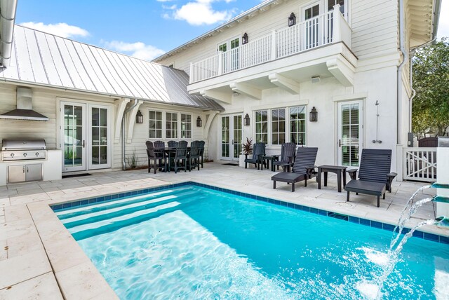 rear view of property with french doors, pool water feature, a balcony, a patio area, and exterior kitchen